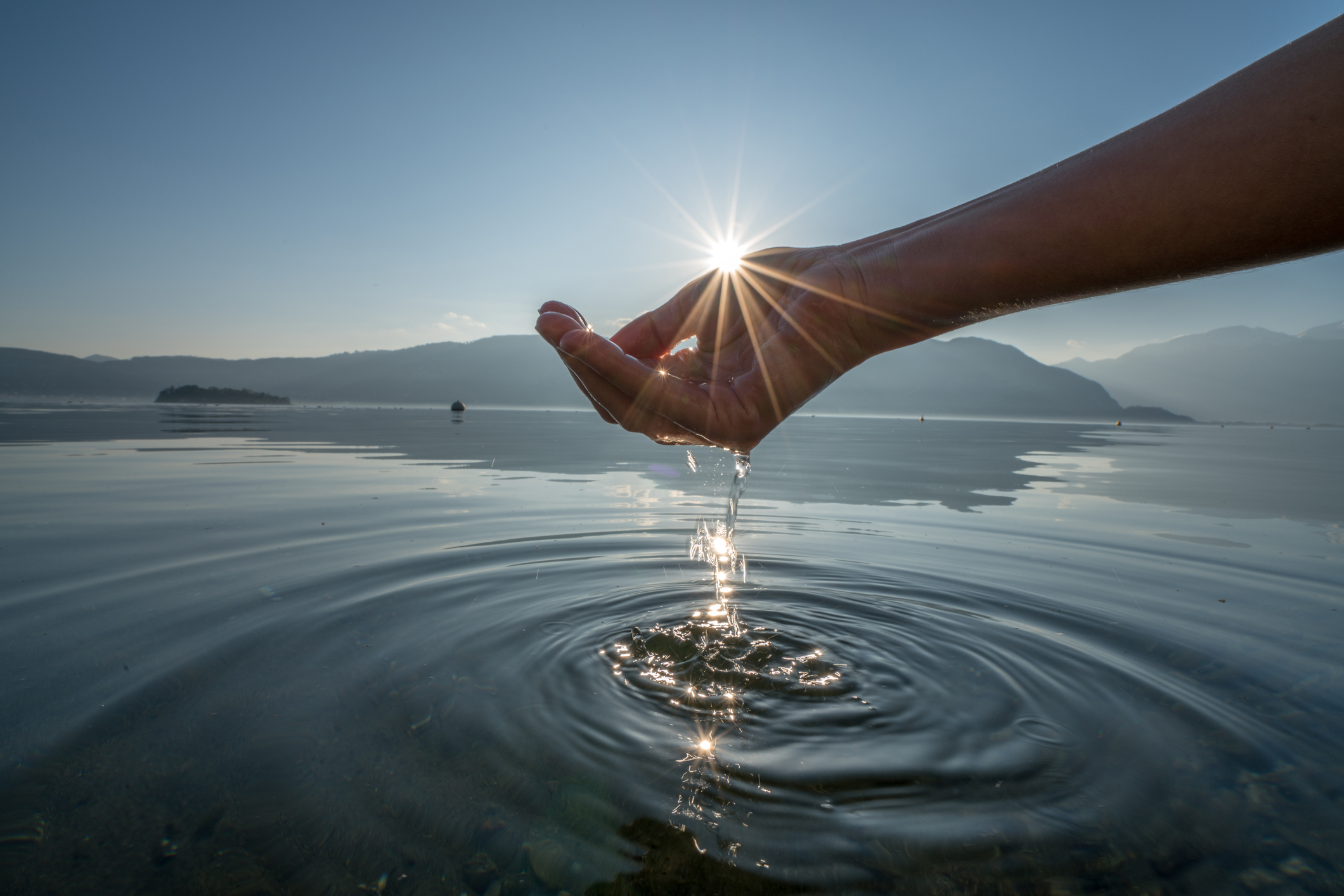 Cupped hands catching water in sunlight, water dripping through the fingers into a lake