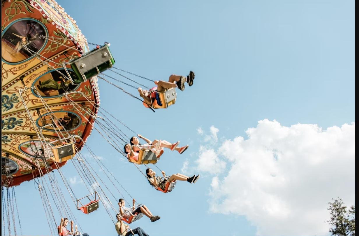 People riding an amusement park swing carousel against a blue sky