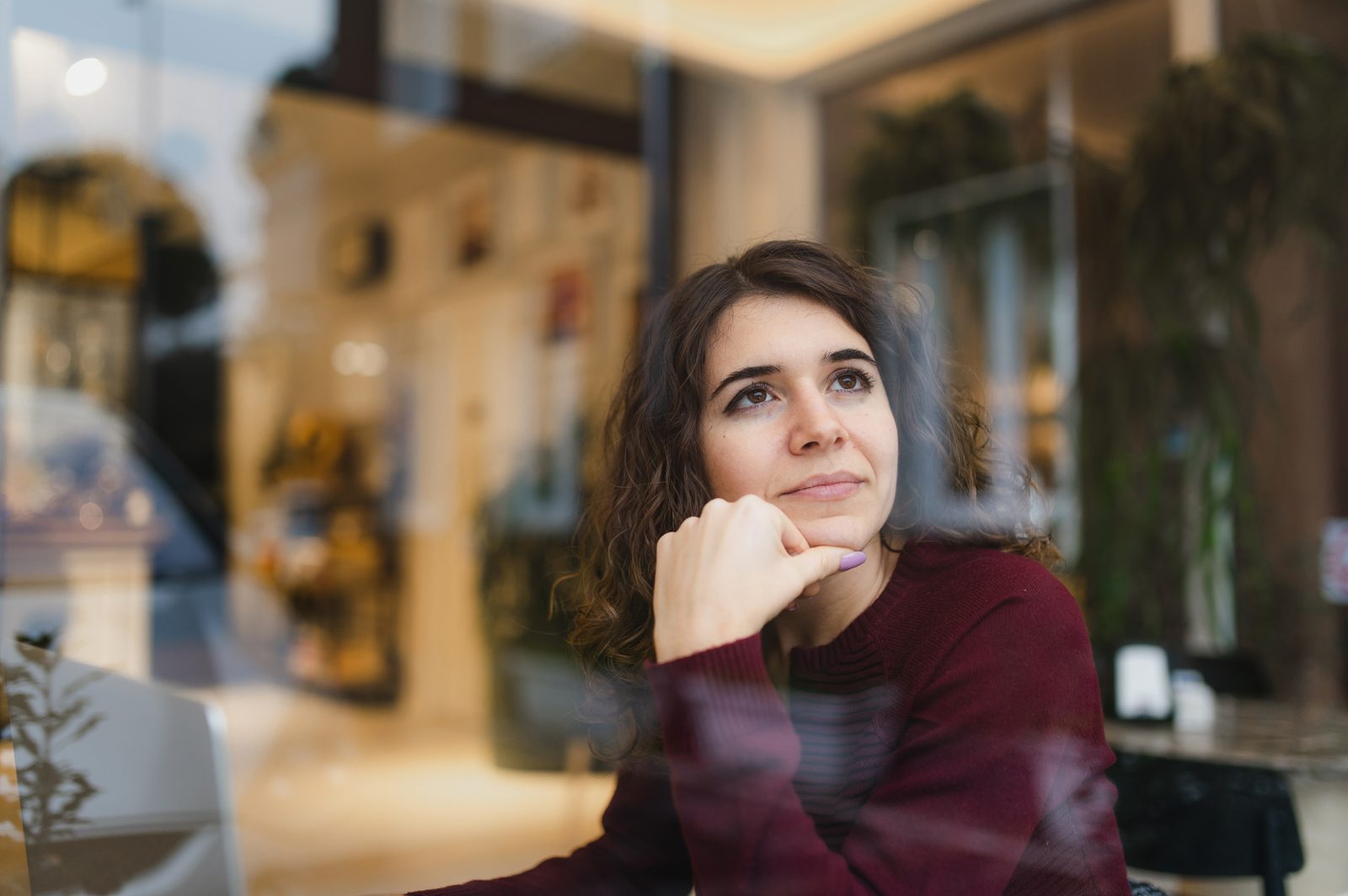 Thoughtful young woman with a café backdrop, wearing a maroon sweater