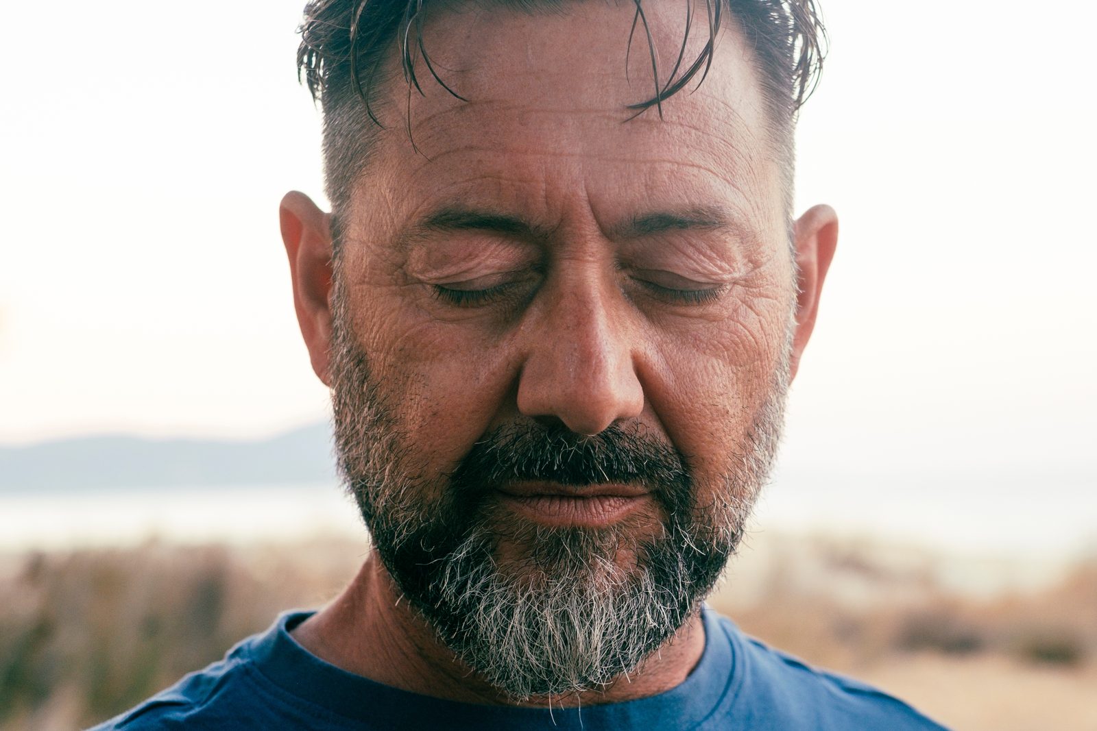 Contemplative man with eyes closed, gray beard, blue shirt