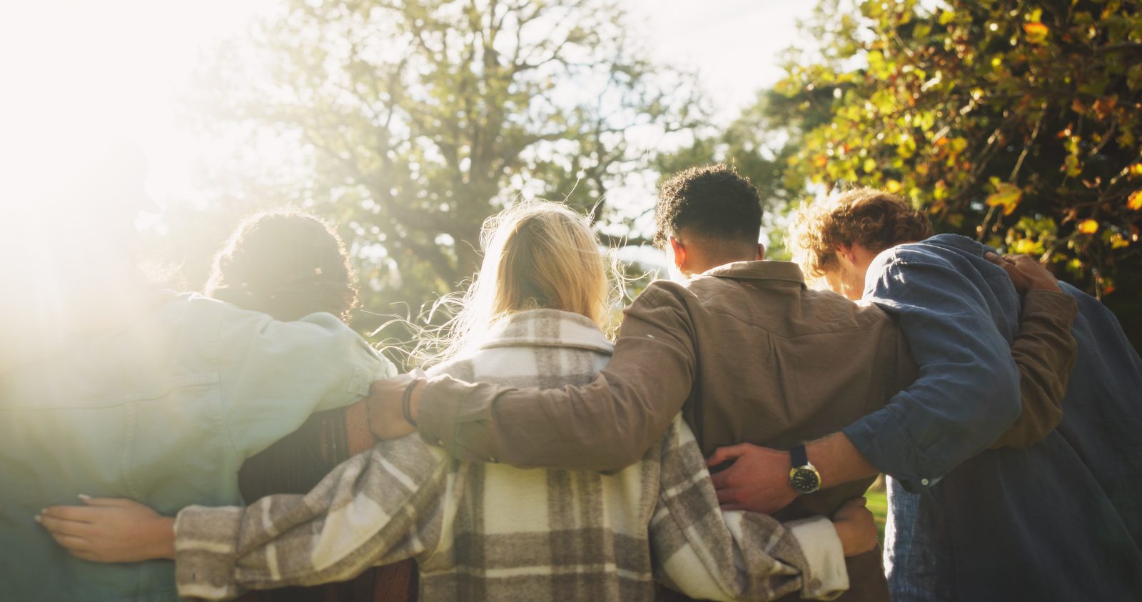 Four friends, backs turned, arms around each other in autumn light